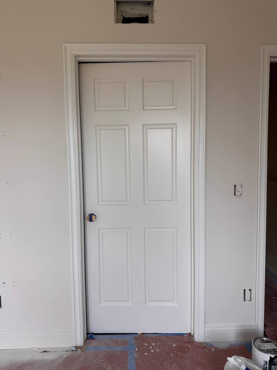 Dark interior door being painted with glass panel masked using blue tape and plastic film Title: Interior Door Painting Process – Mr. Rarov Painting Los Angeles